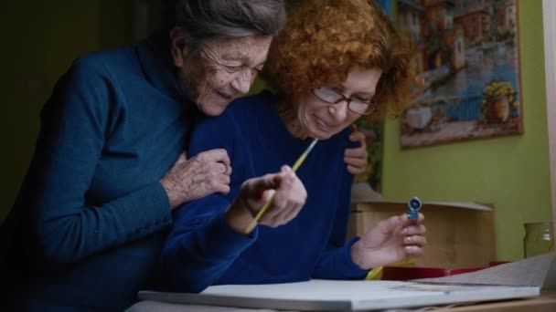 En gammal mamma besöker ett vårdhem. Ritning lektion med en äldre dotter och äldre mor i en konststudio. Gemensam familj hobby av två kvinnor att måla målningar på duk. Måleri verkstad — Stockvideo
