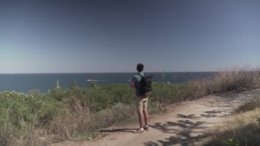 Kafkas erkek turist güneşli yaz havasında dağ yolunda haikin yaparken deniz manzarası seyrediyor. Lycian yolunda yürüyüş. Sırt çantalı gezgin uçurumun kenarında duruyor. Macera, seyahat insanları konsepti