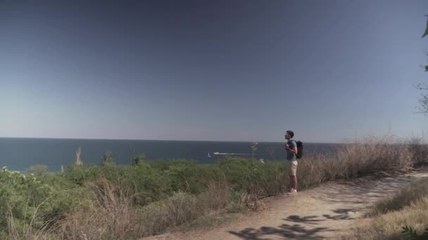在Lycian路上徒步旅行夏天，人们背着背包在海滨和山路上散步，阳光灿烂。提着背包的男性旅行者喜欢看蓝色海水。在海滨远足 — 图库视频影像