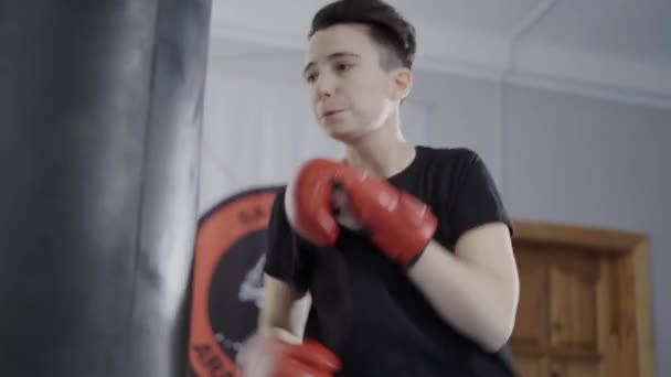 Boxare flicka med boxningshandskar slå den tunga påsen. Träningskvinna med boxningssäck i gymmet. Kvinnlig makt. Kvinna som tränar kampsport. Gittande boxningssäck. Sandsäck är ett par slag — Stockvideo