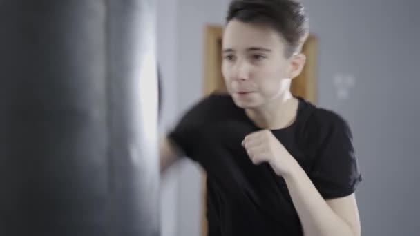 Kickboxing atleta professionista donna calcia il sacco da boxe in palestra. Studente imparare nozioni di base di taekwondo al chiuso. Tenete le mani dentro. L'arte dell'autodifesa. Combattente donna. Sacco da boxe donna atletica — Video Stock