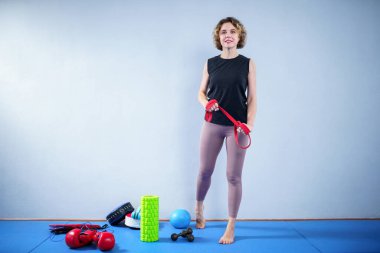 Spor salonunda dirençli elastik bantlarla egzersiz yapan sportif bir kadın. Sporcu kadın elastik bantla egzersiz yapıyor. İnsanlar, spor, fitness konsepti. Güç ve canlılık. Egzersiz için direnç bandı kullanılıyor.