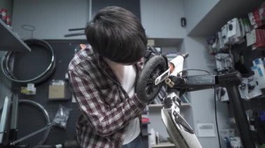 Çevre dostu elektrikli araç tamir servisi. Beyaz erkek elektrikli taşıma tamircisi istasyonda çalışıyor. Tamir ve hizmet için atölyede çalışan adam, elektrik itme scooterını tamir ediyor.
