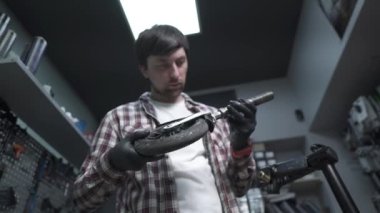 Elektrikli scooter tamir atölyesi. Tamirci elinde çocuk scooter 'ının ve tekerleğinin kırık bir parçasını tutuyor. Modern çevre dostu ulaşım şekli. Tamircide çalışırken tamirci.