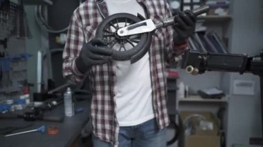 Çevre dostu elektrikli araç tamir servisi. Beyaz erkek elektrikli taşıma tamircisi istasyonda çalışıyor. Tamir ve hizmet için atölyede çalışan adam, elektrik itme scooterını tamir ediyor.