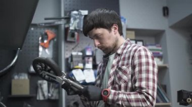 Elektrikli scooter tamir atölyesi. Tamirci elinde çocuk scooter 'ının ve tekerleğinin kırık bir parçasını tutuyor. Modern çevre dostu ulaşım şekli. Tamircide çalışırken tamirci.