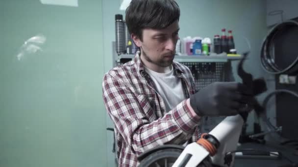 Joven mecánico caucásico trabajando en taller de reparación, arreglando niños patada scooter. Scooter de reparación, servicio de mantenimiento. Transporte ecológico. Reparación de scooter eléctrico en taller especial — Vídeo de stock