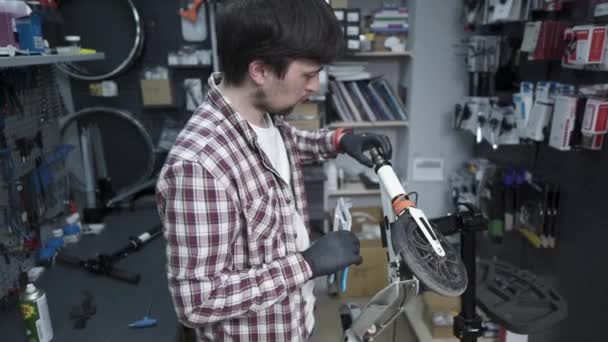 Mężczyzna mechanik, mechanik naprawia mechaniczne uszkodzenia kół dziecięcego skutera. Małe przedsiębiorstwo zajmujące się obsługą i utrzymaniem ekologicznego transportu skuterów. Złamany hulajnoga — Wideo stockowe
