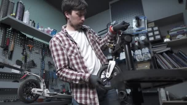 Elektrikli scooter tamir atölyesi. Tamirci elinde çocuk scooter 'ının ve tekerleğinin kırık bir parçasını tutuyor. Modern çevre dostu ulaşım şekli. Tamircide çalışırken tamirci. — Stok video