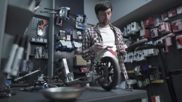 Atölyede elektrikli scooter üzerinde çalışan profesyonel bir zanaatkar. Çocukların tekerleklerini tamir eden teknisyenler tamir atölyesinde scooter satıyorlar. Tamirci işte. Çevre dostu nakliye aracı. Scooter bakım servisi — Stok video