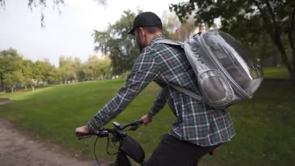 Vždy cestovat domácí mazlíček a majitel společně. Cyklista nese mladou šedou kočku ve speciálním batohu se zvířecím mazlíčkem s oknem a větráním na kole. Téma horské kolo jízda s kočkou v tašce na zádech — Stock video