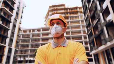 Koronavirüs, covid-19, hava kirliliği, toz, inşaat ve imalatta alerji. Çalışanların sağlık koruması. İnşaatçı inşaat alanında kask takar ve 95 numaralı koruyucu maskeyi takar..