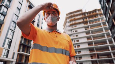 Koronavirüs, covid-19, hava kirliliği, toz, inşaat ve imalatta alerji. Çalışanların sağlık koruması. İnşaatçı inşaat alanında kask takar ve 95 numaralı koruyucu maskeyi takar..