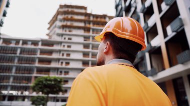 Konu, üretim ve inşaatta sağlığın korunması. Turuncu üniformalı ve koruyucu solunum cihazlı beyaz erkek işçi inşaat turuncu kaskını takıyor ve inşaat alanında poz veriyor..