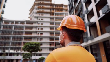 Koronavirüs, covid-19, hava kirliliği, toz, inşaat ve imalatta alerji. Çalışanların sağlık koruması. İnşaatçı inşaat alanında kask takar ve 95 numaralı koruyucu maskeyi takar..