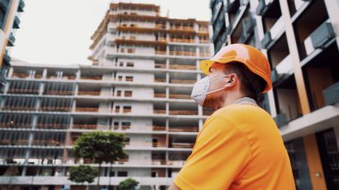 Koronavirüs, covid-19, hava kirliliği, toz, inşaat ve imalatta alerji. Çalışanların sağlık koruması. İnşaatçı inşaat alanında kask takar ve 95 numaralı koruyucu maskeyi takar..