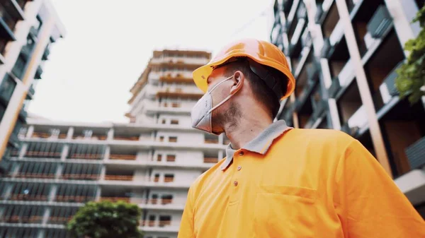 Koronavirüs, covid-19, hava kirliliği, toz, inşaat ve imalatta alerji. Çalışanların sağlık koruması. İnşaatçı inşaat alanında kask takar ve 95 numaralı koruyucu maskeyi takar..