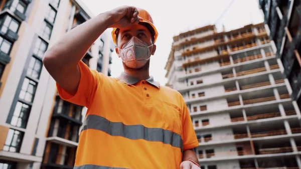 Koronavirüs, covid-19, hava kirliliği, toz, inşaat ve imalatta alerji. Çalışanların sağlık koruması. İnşaatçı inşaat alanında kask takar ve 95 numaralı koruyucu maskeyi takar..