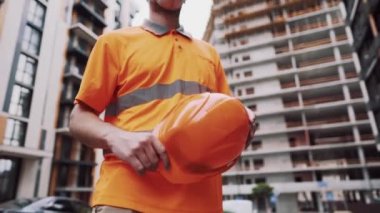 Konu, üretim ve inşaatta sağlığın korunması. Turuncu üniformalı ve koruyucu solunum cihazlı beyaz erkek işçi inşaat turuncu kaskını takıyor ve inşaat alanında poz veriyor.
