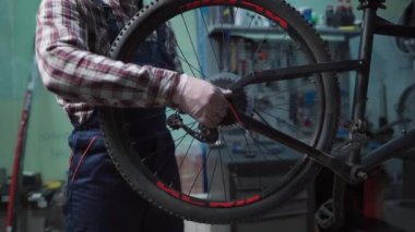 Tamirhanede bisiklet tamircisi bisiklet tekerleğini tamir ediyor. Velocipede servisi. Tamirci erkek bisikletçi atölyede bisiklet tekerleğini tamir ediyor. Teknisyen bisiklet parçalarını tamir ediyor. İş yerindeki tamirci.