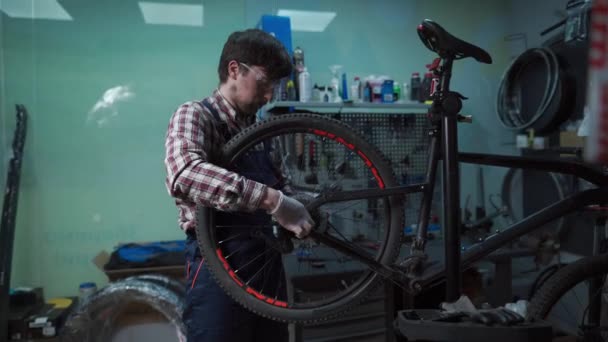 Young caucasian repairman repairing mountain bike wheel in bike shop workshop. Fixing bicycle. Caring for you wheels. man mechanic working in garage. Worker fixing cycle gear. Small business theme — Stock Video