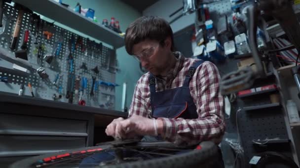 Bicycle mechanic fixing cycle wheel in repair shop. Velocipede service. Repairer male bike shop engineer fix bicycle wheel in workshop. Technician fixes bike parts. Handyman at work in the workplace — Stock Video