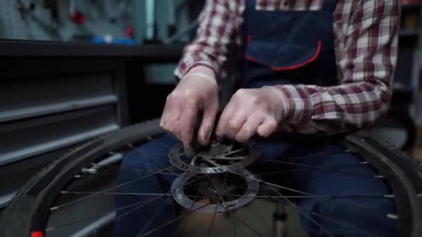 Mecânico masculino trabalhando na loja de reparação de bicicletas, mecânico de reparação de bicicleta usando ferramenta especial, usando luvas de proteção. Jovem atraente serviceman fixação clientes roda de bicicleta em sua própria oficina — Vídeo de Stock