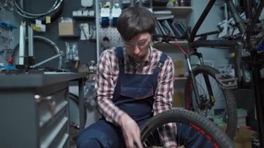Tamirhanede bisiklet tamircisi bisiklet tekerleğini tamir ediyor. Velocipede servisi. Tamirci erkek bisikletçi atölyede bisiklet tekerleğini tamir ediyor. Teknisyen bisiklet parçalarını tamir ediyor. İş yerindeki tamirci.