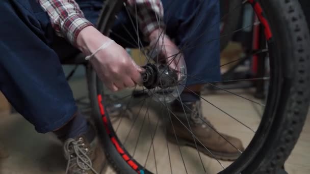 Męski mechanik pracujący w warsztacie rowerowym, mechanik naprawiający rower przy użyciu specjalnego narzędzia, noszący rękawice ochronne. Młody, atrakcyjny serwisant naprawiający koła rowerowe klientów we własnym warsztacie — Wideo stockowe