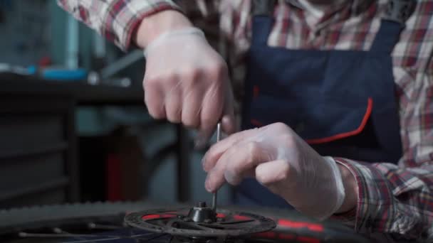 Mecánico masculino que trabaja en taller de reparación de bicicletas, mecánico que repara la bicicleta usando la herramienta especial, usando guantes protectores. Joven hombre de servicio atractivo fijación de clientes rueda de bicicleta en su propio taller — Vídeos de Stock