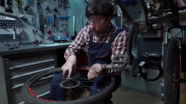 Technical expertise taking care bicycle shop. Handsome young mechanic fixing cycle wheel in workshop. Handsome repairman in workwear serving mountain bicycle. Male engineer adjusting velocipede — Stock Video