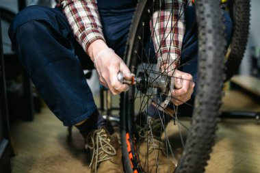 Tamirhanede bisiklet tamircisi bisiklet tekerleğini tamir ediyor. Velocipede servisi. Tamirci erkek bisikletçi atölyede bisiklet tekerleğini tamir ediyor. Teknisyen bisiklet parçalarını tamir ediyor. İş yerindeki tamirci..