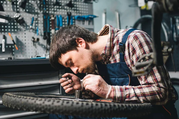 Young caucasian repairman repairing mountain bike wheel in bike shop workshop. Fixing bicycle. Caring for you wheels. man mechanic working in garage. Worker fixing cycle gear. Small business theme.