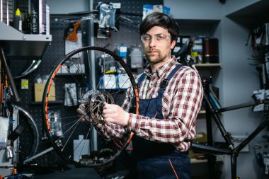 Bisiklet tamirhanesinde teknik uzmanlık. Atölyede bisiklet tekerleğini tamir eden yakışıklı genç bir tamirci. Dağ bisikletine servis yapan iş elbisesi tamircisi. Erkek mühendis hızını ayarlıyor..