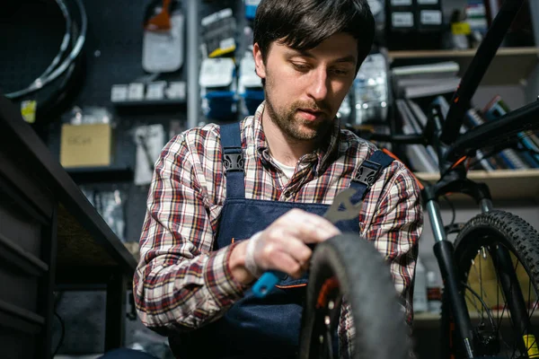 Technical expertise taking care bicycle shop. Handsome young mechanic fixing cycle wheel in workshop. Handsome repairman in workwear serving mountain bicycle. Male engineer adjusting velocipede.