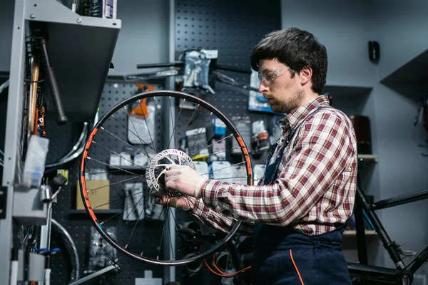 Technical expertise taking care bicycle shop. Handsome young mechanic fixing cycle wheel in workshop. Handsome repairman in workwear serving mountain bicycle. Male engineer adjusting velocipede.
