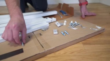 Yeni eve taşınıyorum. Kutuları açmak ve mobilyaları monte etmek. Adam talimatları okuyor ve mobilyaları monte ediyor. DIY. Erkek, yeni beyaz mobilyalar kuruyor. Kendiniz yapın. Mobilya montaj süreci