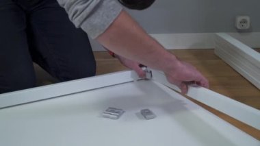 Yeni eve taşınıyorum. Kutuları açmak ve mobilyaları monte etmek. Adam talimatları okuyor ve mobilyaları monte ediyor. DIY. Erkek, yeni beyaz mobilyalar kuruyor. Kendiniz yapın. Mobilya montaj süreci