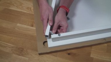 Genç beyaz adam talimatları kullanarak beyaz mobilyaları düz kutudan topluyor. Erkek, karantina sırasında online DIY almış. Coronavirus 'u kilitleyin. Mobilyaları ev ve kendi kendine monte edin.