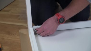 Genç beyaz adam talimatları kullanarak beyaz mobilyaları düz kutudan topluyor. Erkek, karantina sırasında online DIY almış. Coronavirus 'u kilitleyin. Mobilyaları ev ve kendi kendine monte edin.