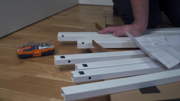 DIY witte tafel assemblage proces thuis. Meubelinstallatie. Nieuw huis en de man die meubels monteert doen het zelf. Mannelijke montagetafel uit doos volgens de instructies op de vloer — Stockvideo