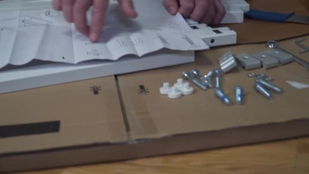 Jonge blanke man monteert witte meubels uit platte doos met behulp van instructies. Man kocht tafel online DIY tijdens quarantaine covid 19. Afsluiting coronavirus bestellen meubels thuis en zelf-assemblage — Stockvideo