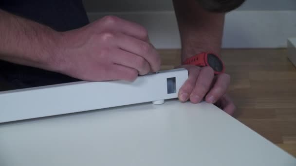 Hombre montando muebles de paquete plano DIY en casa en el suelo. El hombre compró muebles a través de la tienda en línea, se ensambla mesa según las instrucciones durante la cuarentena coronavirus. Pedir muebles a casa — Vídeos de Stock