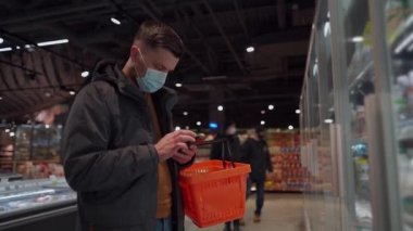 Markette alışveriş yapan, alışveriş sepetiyle yürüyen, süpermarkette karantina sırasında gerekli malzemeleri alan, koruyucu maske takan bir adam. Yeni normal, covid 19 ve alışverişler. Maske yoksa giriş de yok