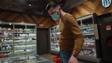 Markette alışveriş yapan, alışveriş sepetiyle yürüyen, süpermarkette karantina sırasında gerekli malzemeleri alan, koruyucu maske takan bir adam. Yeni normal, covid 19 ve alışverişler. Maske yoksa giriş de yok