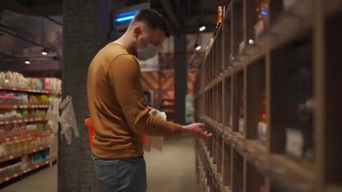 Markette koruyucu maske takan genç bir adam. Tıbbi maskeli bir erkek müşteri karantina koronavirüsü sırasında markette süt ürünlerini seçiyor. Yeni kural, maske girdisi yok