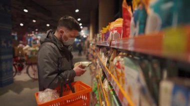 Sağlık, güvenlik alışverişi ve salgın hastalık konsepti. Maskeli bir adam marketten yiyecek alıyor. Tedbirleri alın ve engelleyin. Süpermarkette maske takan genç bir erkek el arabasıyla alışveriş yapıyor. Covid 19