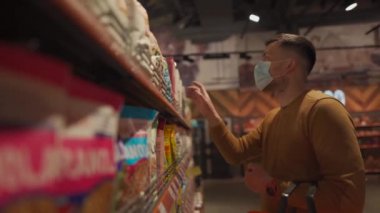 Markette alışveriş yapan, alışveriş sepetiyle yürüyen, süpermarkette karantina sırasında gerekli malzemeleri alan, koruyucu maske takan bir adam. Yeni normal, covid 19 ve alışverişler. Maske yoksa giriş de yok