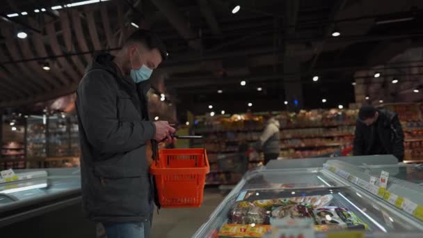 Koncepcja zdrowia, bezpieczeństwa zakupów i pandemii. Klient w masce kupuje jedzenie w spożywczaku. Ochrona i zapobieganie środkom. Młody mężczyzna w masce na twarz zakupy w supermarkecie z wózkiem. Żółw 19 — Wideo stockowe