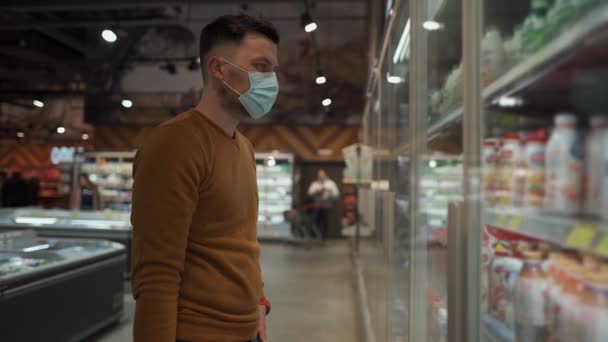 Joven con mascarillas protectoras en la tienda de comestibles. Cliente masculino en mascarilla médica eligiendo productos lácteos en el supermercado durante la cuarentena coronavirus. Nueva regla, sin entrada de máscara — Vídeos de Stock